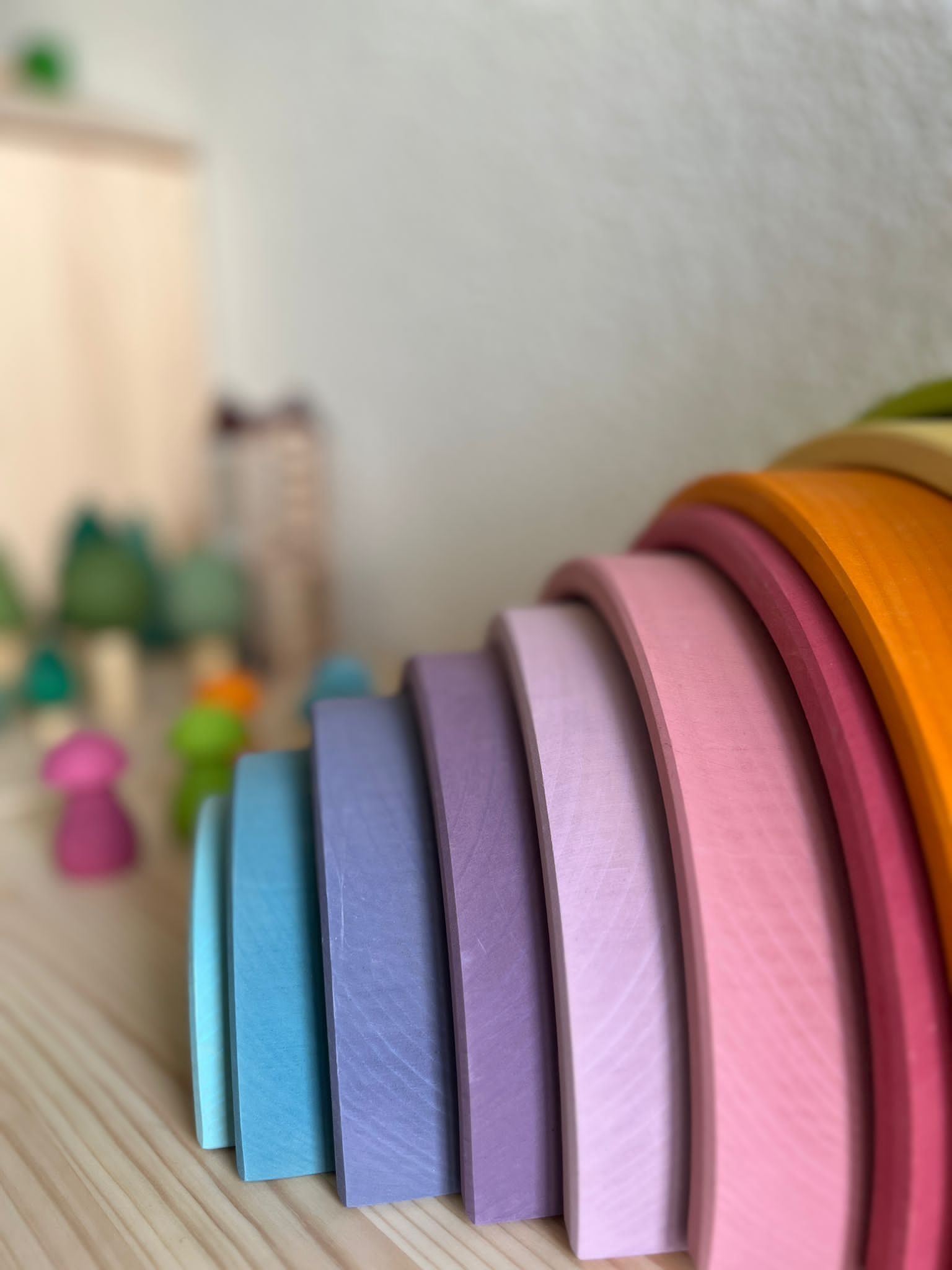Holzregenbogen in Pastellfarben, davor Holzpilze